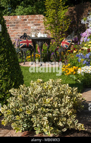 Fleurs colorées, pelouse, patio & thé pour deux personnes dans quartier calme ensoleillé - un reflet de sa 'Vie' show garden, RHS Flower Show, Tatton Park, Angleterre, Royaume-Uni. Banque D'Images