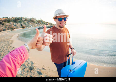 Jeune homme arrivant à la station et debout sur la plage tandis que showing Thumbs up Banque D'Images