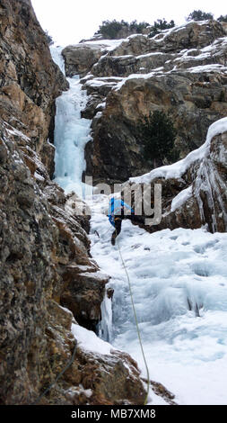 Grimpeur sur glace masculin dans une veste bleue sur une magnifique cascade de glace escalade dans les Alpes en hiver profonde Banque D'Images