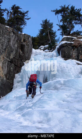 Grimpeur sur glace masculin dans une veste bleue sur une magnifique cascade de glace escalade dans les Alpes en hiver profonde Banque D'Images