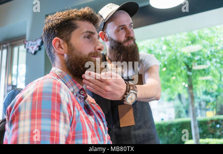 Jeune homme barbu pense à un changement de look dans le salon de coiffure Banque D'Images