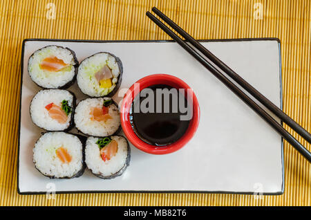 Sommaire des six rouleaux de sushi sur une assiette avec un bol de sauce soja et baguettes Banque D'Images