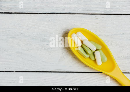 Assortiment de comprimés, comprimés et capsules en jaune sur la cuillère en bois. Banque D'Images