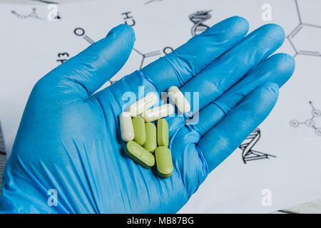Assortiment de comprimés, comprimés et capsules sur la main dans le gant bleu contre fond blanc avec des formules chimiques. Banque D'Images