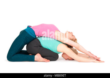 Vue complète du corps de deux jeunes femmes blondes en un partenaire les exercices du Yoga lying on floor in front of white background avec des ombres. Banque D'Images