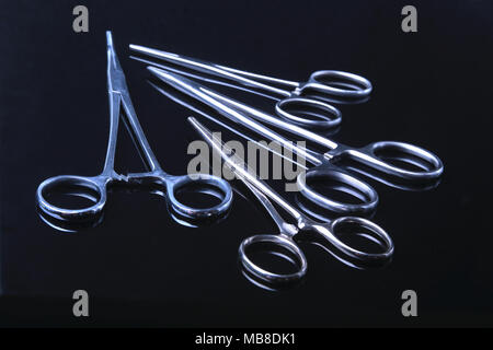 Les instruments chirurgicaux et d'outils, notamment de scalpels, forceps et la pince noire sur fond de miroir Banque D'Images