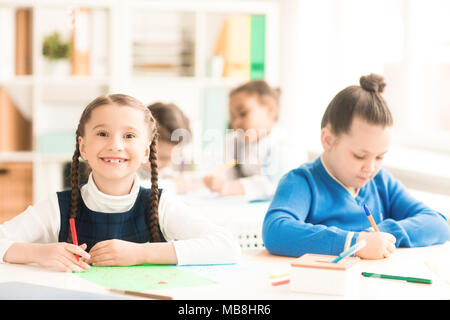 Portrait of smiling schoolgirl assis au bureau avec son classmte et dessin Banque D'Images