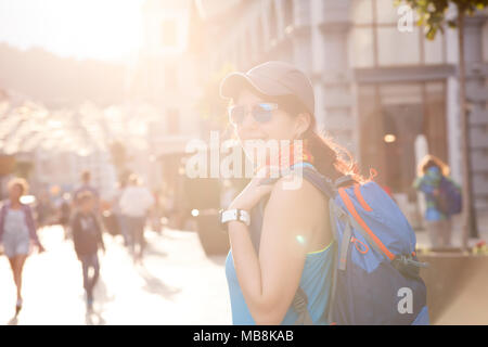 Image de femme souriante avec sac à dos sur fond flou des édifices de la ville avec des personnes sur la journée d'été Banque D'Images