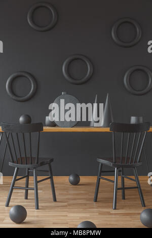 Sculptures en bois rond et en forme de cône placé sur le sol et une table de salle à manger en noir intérieur avec deux chaises Banque D'Images