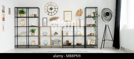 Close-up de racks métalliques avec décorations debout contre un mur blanc avec horloge ronde à l'intérieur salon lumineux Banque D'Images