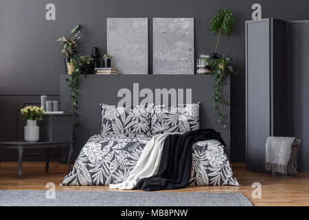 Literie floral noir et blanc sur le lit avec deux couvertures debout dans une pièce sombre avec des peintures à l'intérieur simple et plantes fraîches Banque D'Images