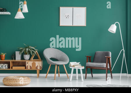 Tabouret blanc entre les fauteuils gris contre mur vert avec des affiches dans le salon intérieur avec pouf Banque D'Images