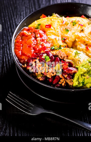 Nachos au fromage fondu, le guacamole et les haricots rouges sur fond sombre, prêt à manger Banque D'Images