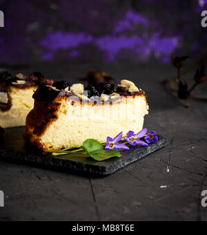 Un morceau de gâteau au fromage sur un fond noir parsemé de copeaux secs et amandes cerises, Close up Banque D'Images