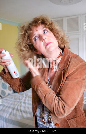 Femme mature d'âge moyen à l'aide de la laque pour cheveux sur cheveux bouclés blonds prêt pour sortir le soir cendres photographie prise par Simon Dack Banque D'Images