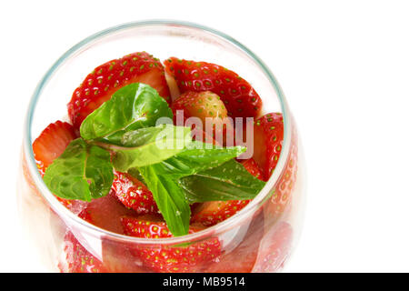 Couper les fraises avec les feuilles de menthe dans un verre isolé sur fond blanc Banque D'Images