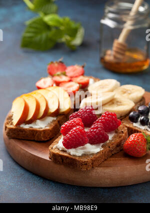 Petit-déjeuner diététique. Toasts avec du fromage à la crème et les baies fraîches et fruits : banane, bleuet, framboise, fraise, pêche. Banque D'Images