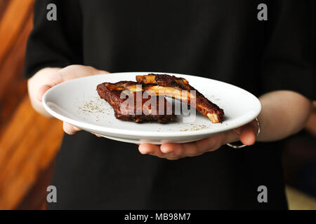 Boeuf fumé épicé côtelettes de porc au four avec des épices et du poivre côtes snack-à la bière en plaque blanche dans les mains du serveur Banque D'Images