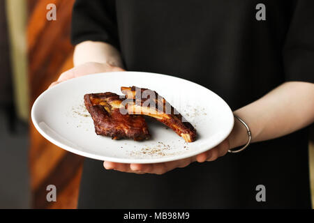 Boeuf fumé épicé côtelettes de porc au four avec des épices et du poivre côtes snack-à la bière en plaque blanche dans les mains du serveur Banque D'Images