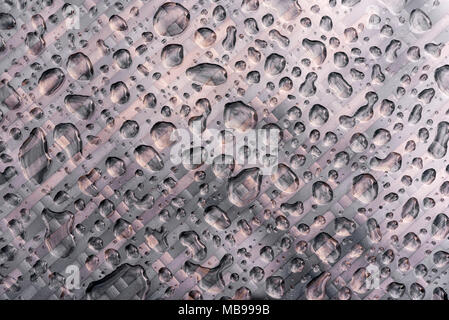 Vue de dessus de gouttelettes de pluie sur une table de jardin en rotin recouvert de verre, après une forte pluie. Banque D'Images