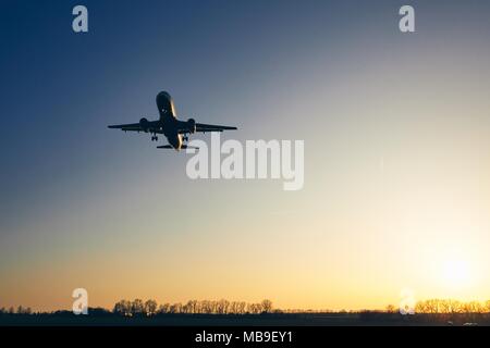 Silhouette de l'atterrissage de l'avion contre moody sky au coucher du soleil doré. Banque D'Images
