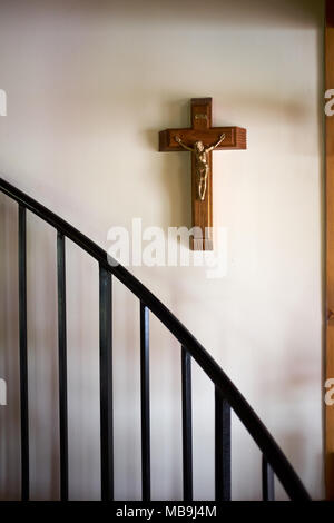 Crucifix en bois avec la figure du Christ crucifié accroché sur un mur intérieur blanc avec rampe d'escalier Banque D'Images