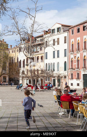 Campo San Polo, San Polo, Venise, Vénétie, Italie au printemps avec une petite fille courir après les oiseaux et les hommes de salle dans un restaurant et reposant sur des bancs Banque D'Images