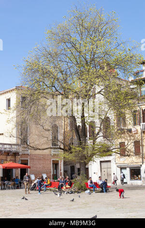 Campo San Polo, San Polo, Venise, Vénétie, Italie au printemps avec des familles et leurs enfants profiter de la soleil du printemps sur la banquette rouge Banque D'Images