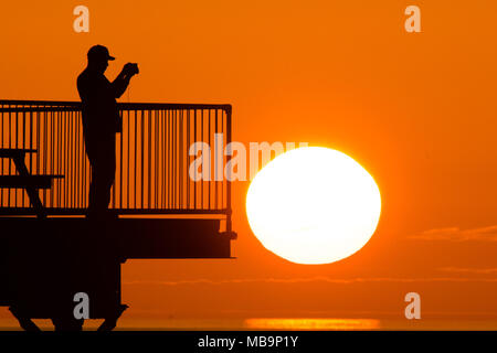 Pays de Galles Aberystwyth UK, dimanche 08 avril 2018 Météo France : Un homme se tient et photos à la fin de la station balnéaire d'Aberystwyth tronqué jetée au coucher du soleil magnifique sur la baie de Cardigan, à la fin, un jour de printemps chaud et ensoleillé sur la côte ouest de l'UK Photo © Keith Morris / Alamy Live News Banque D'Images