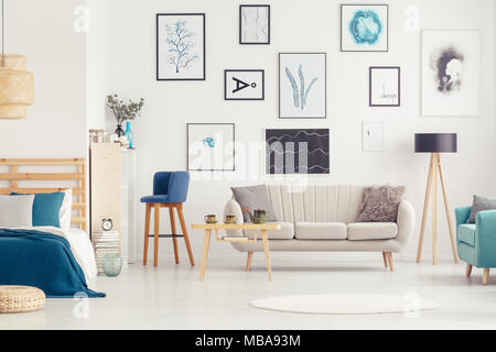 Tabouret de bar bleu à côté du canapé et table en bois dans un espace libre intérieur avec des affiches et des chambres Banque D'Images