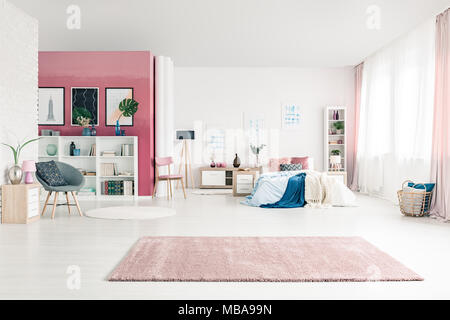 L'espace ouvert de l'intérieur chambre à coucher avec grand lit confortable, tapis, murs blancs et roses, des chaises, des affiches, panier, rideaux rose et bibliothèques Banque D'Images