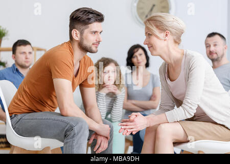 Jeune homme et femme d'âge moyen assis et se regarder dans les yeux avec d'autres personnes dans l'arrière-plan Banque D'Images