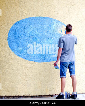 Jeune homme peint ovale bleu sur un mur de béton. L'artiste graffiti mâles adultes peint le mur. Street art urbain en plein air concept. Place pour le texte Banque D'Images