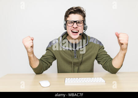 La technologie, jeux, animation, let's play et personnes concept - heureux jeune homme à lunettes avec casque jouant et gagnant le jeu de l'ordinateur à la maison Banque D'Images