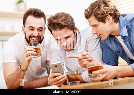 Cheerful friends having fun avec le smartphone et de boire à la maison Banque D'Images