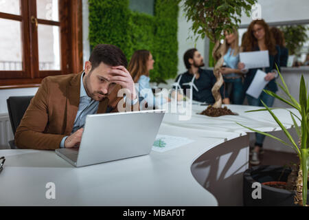 Beau jeune homme pensif inquiète l'analyse des plans d'affaires et de travail sur l'ordinateur portable dans le bureau. Banque D'Images