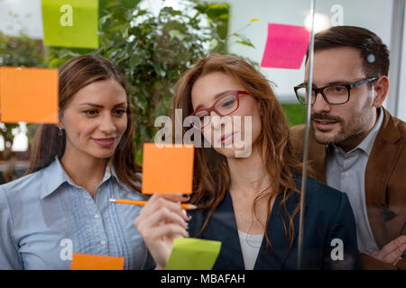 Les professionnels de la création et l'examen permanent au bureau derrière un mur de verre avec des notes adhésives et à un mur de post-it. Banque D'Images