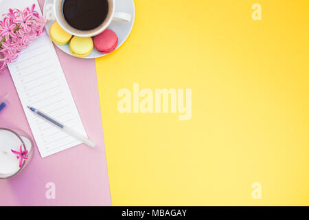 Télévision créative fixer photo de tasse de café avec des macarons et un bloc-notes avec copie espace sur fond jaune et rose style minimal Banque D'Images