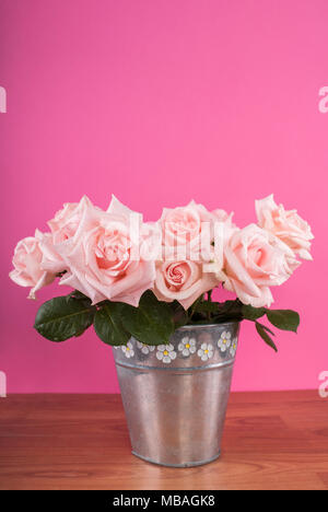 Bouquet de roses en pot de fleurs sur la table et fond rose Banque D'Images