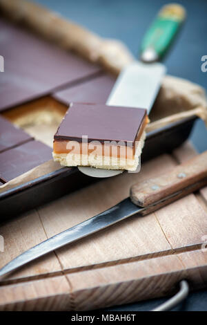 Sablés au caramel / millionnaires shortbread carré sur un couteau sur une planche à découper en bois Banque D'Images