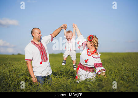 Portrait de famille souche ukrainienne portant des vêtements blancs traditionnels. Père, mère et petit bébé s'amuser à l'extérieur à été ensoleillé terrain. Horizo Banque D'Images