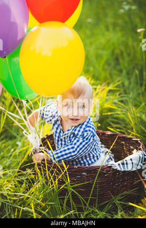 Belle funny little child wearing blue shirt assis à panier décoré avec des ballons à air fond nature. Blonde caucasian baby rechercher Banque D'Images