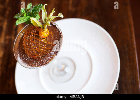 D'un coup horizontal tiramisu se prépare dans un verre à martini, décoré d'un caramel et dom. alchechengi servi sur une plaque blanche sur une table en bois foncé Banque D'Images