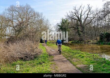 Mâle et femelle Walker cycliste par la rivière Wey navigation sur une journée de printemps ensoleillée près de Ripley, Surrey England UK Banque D'Images