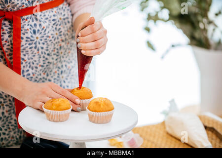 Un petit gâteau de remplissage mains confiseur avec sirop de fraise à l'aide d'une poche à pâtisserie. Banque D'Images