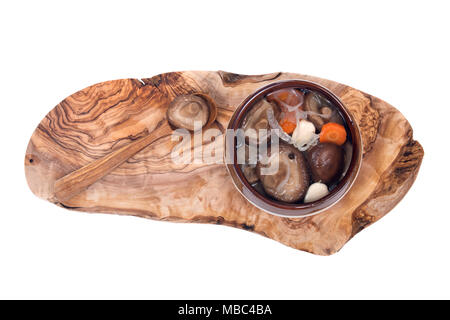 Champignons Shiitake, champignons marinés dans un bol en céramique avec cuillère de bois sur une planche à découper en bois d'olivier isolé sur fond blanc Banque D'Images