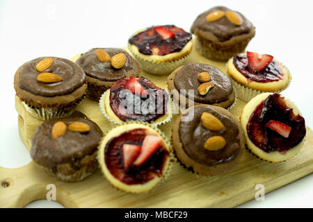 Mini cupcakes avec glaçage au chocolat et garnitures aux amandes et aux fraises disposées sur une planche de bois, lumineuses et appétissantes sur fond blanc Banque D'Images