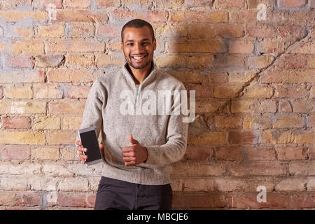 Un beau jeune homme heureux showing Thumbs up avec son smartphone à l'écran dans un pull. Banque D'Images
