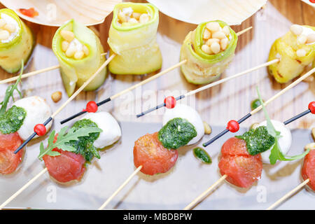 Rouleaux de courgettes avec les pignons de pin. Tomates cerise, mozzarella et basilic sur des brochettes. . Sauce Pesto. Table de buffet savoureux. Fête de l'été à l'extérieur. Banque D'Images