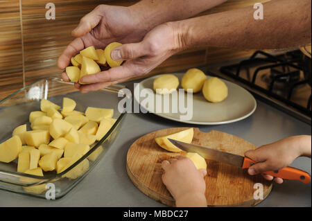 La cuisson à la cuisine. Mains de l'enfant, couper les pommes de terre au couteau. Mettre les morceaux de pommes adultes mains dans le récipient. Banque D'Images